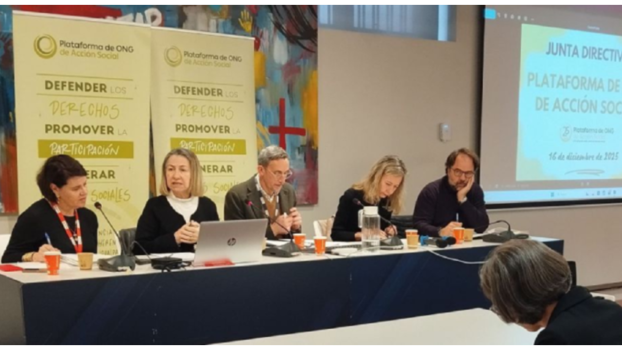 Cinco personas en una mesa presidencial hablando y escribiendo con dos roll up de la Plataforma de ONG detrás