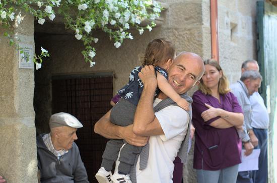 Un hombre sonríe y coge en brazos a una niña pequeña con un grupo de gente alrededor