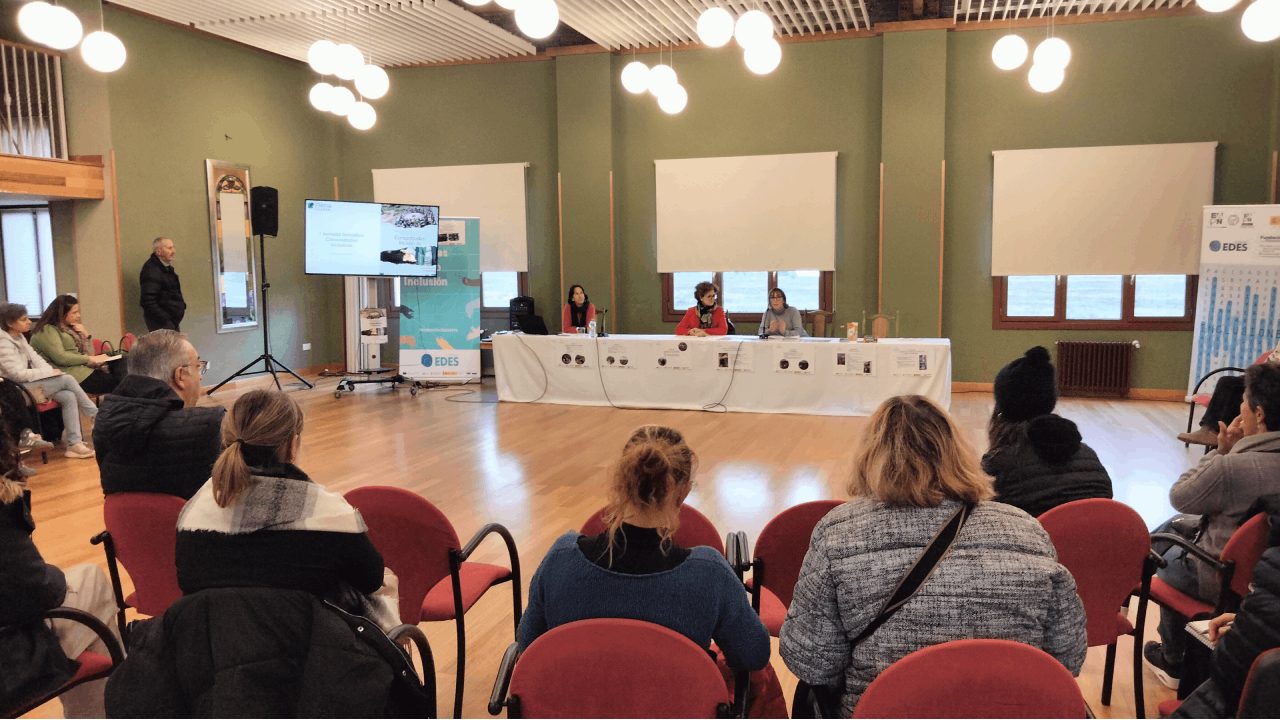 Un grupo de personas sentadas escucha a unas mujeres hablando en una mesa 