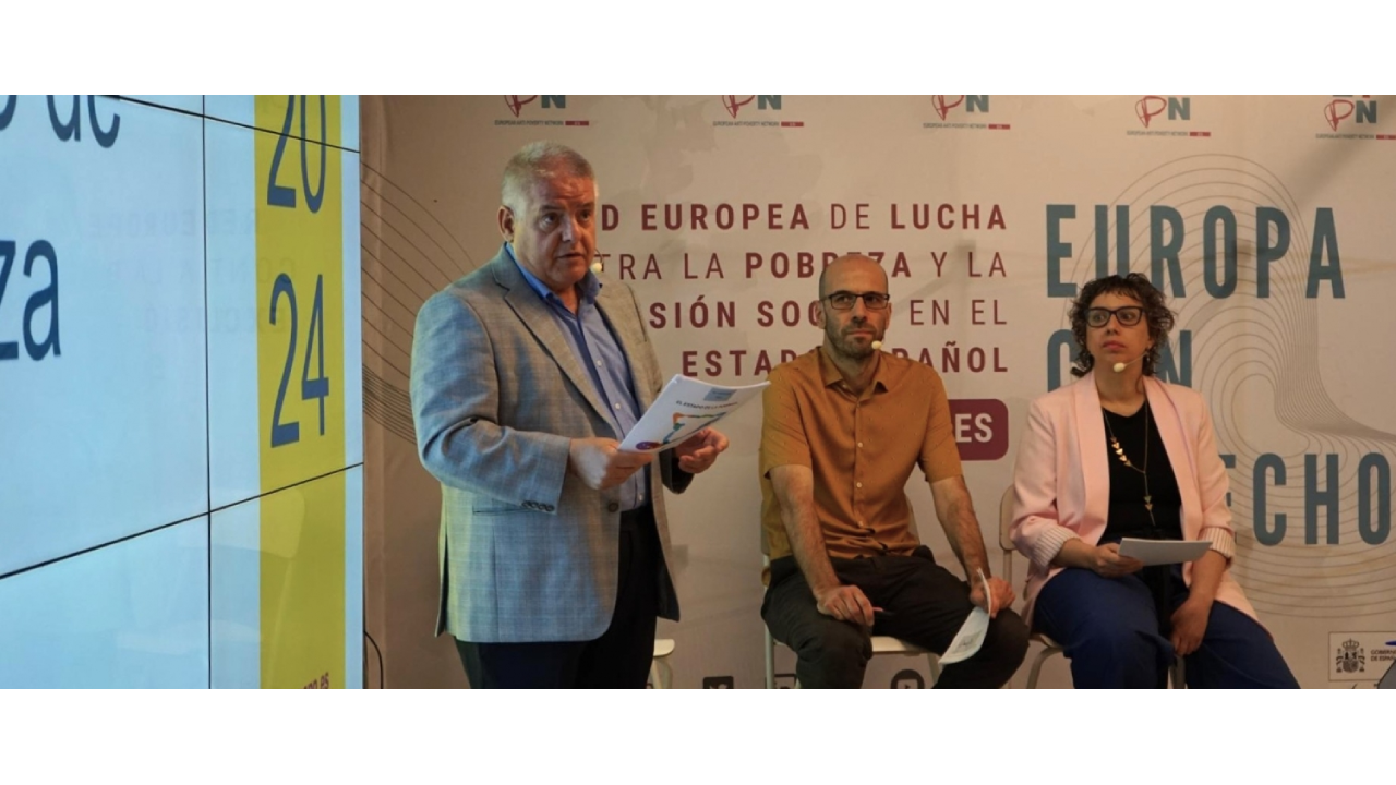 Un hombre con unos papeles de pie habla al lado de dos personas sentadas