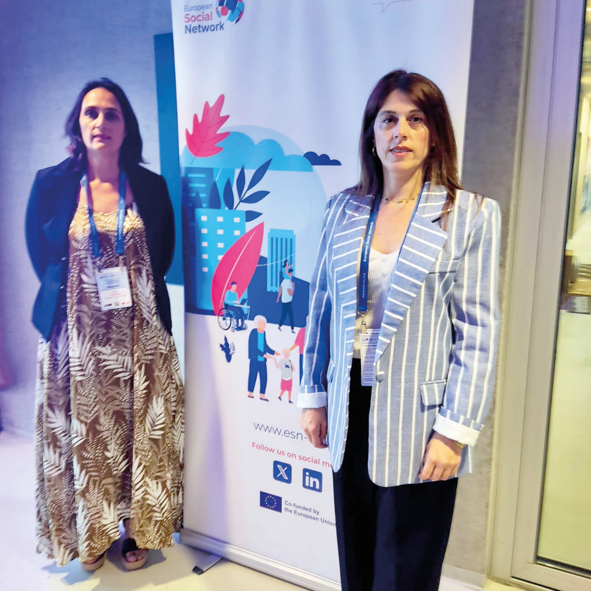 Dos mujeres de pie junto a un cartel de la European Social Services Conference