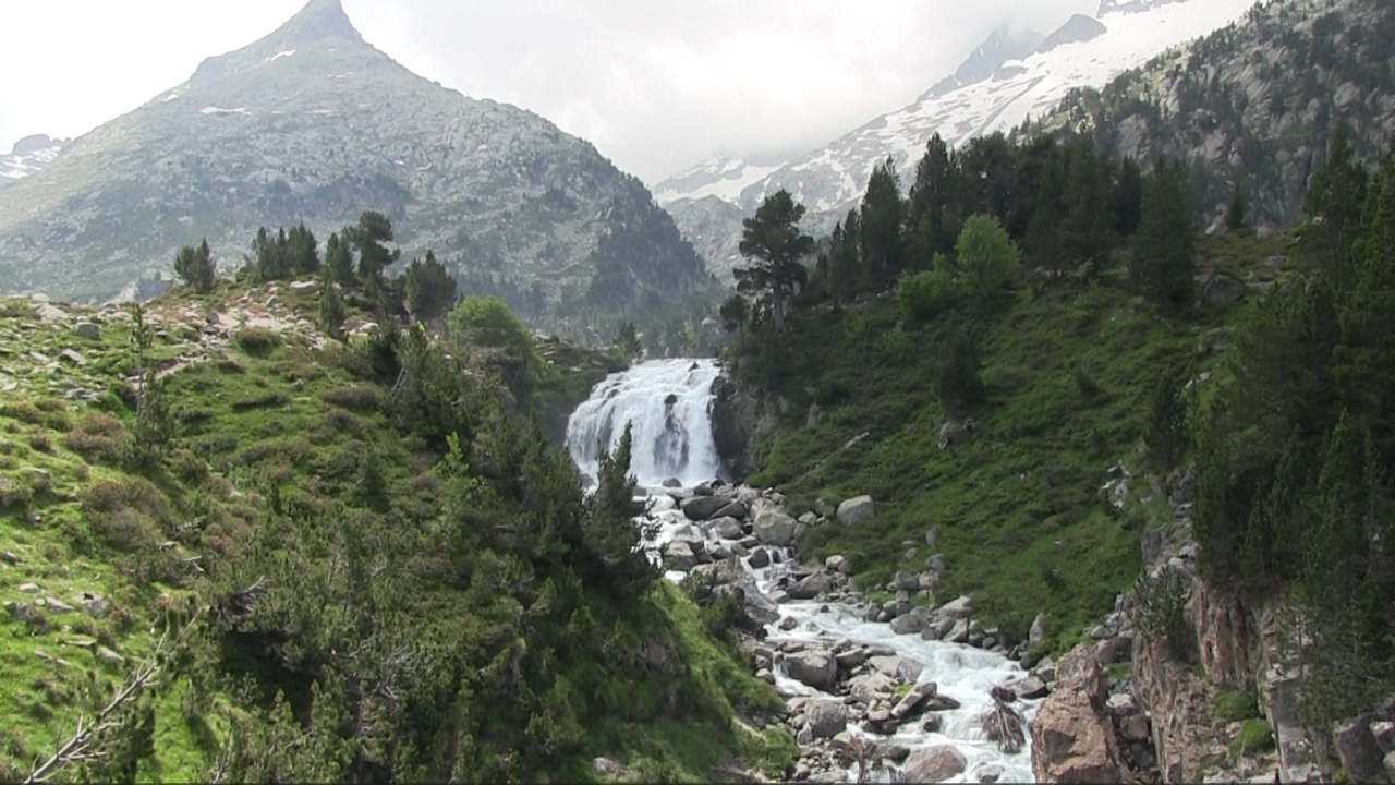Plano general de una cascada que cae y de fondo las montañas nevadas de los Pirineos