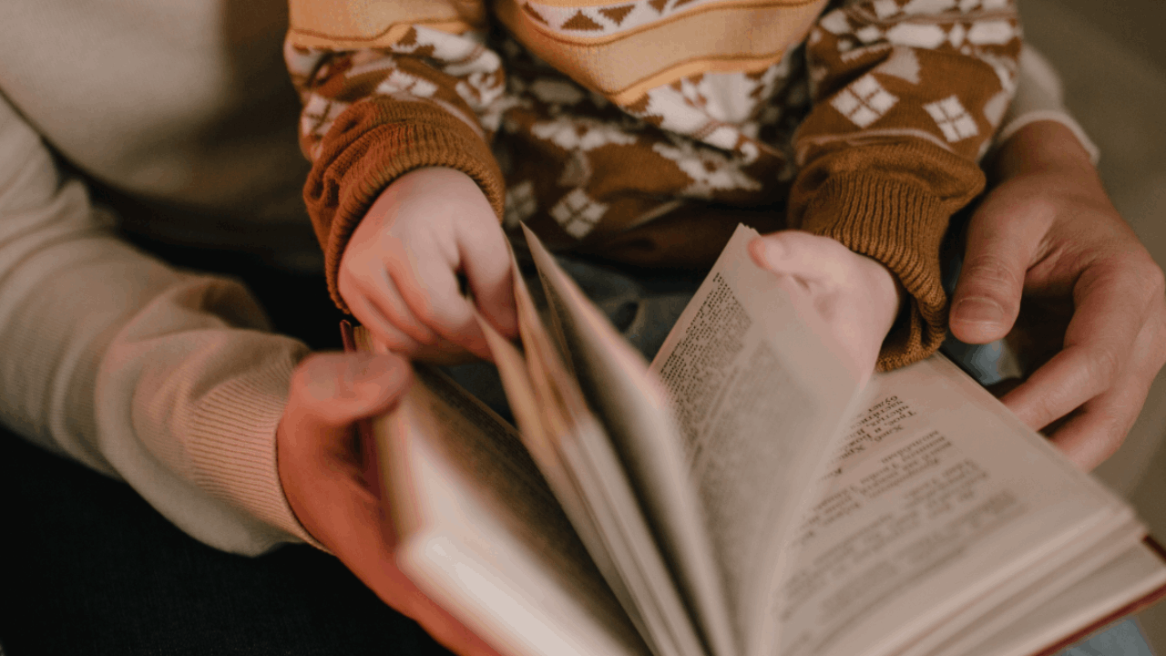 unas manos de un adulto con un niño en brazo leyendo un libro