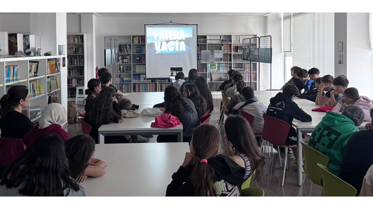 Un grupo de jóvenes sentados en unas mesas viendo una pantalla 