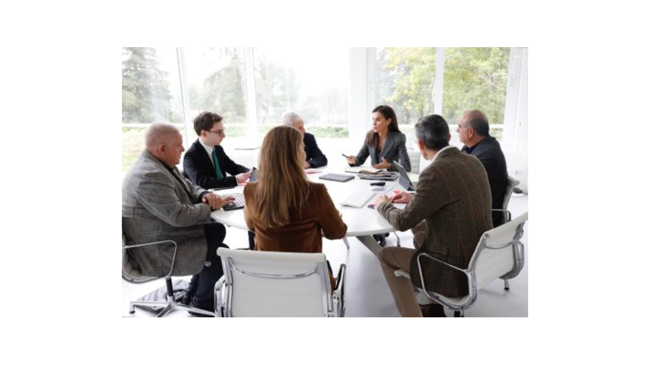 Reunión de varios hombres y mujeres, entre ellas, la Reina, sentados alrededor de una mesa