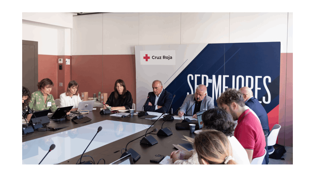 Reunión de personas sentadas alrededor de una mesa y un cartel que pone Ser mejores