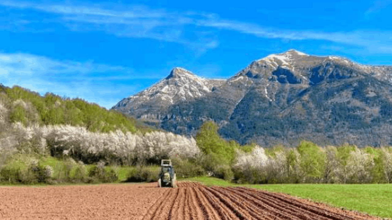 paisaje con montañas y un tractor trabajando la tierra